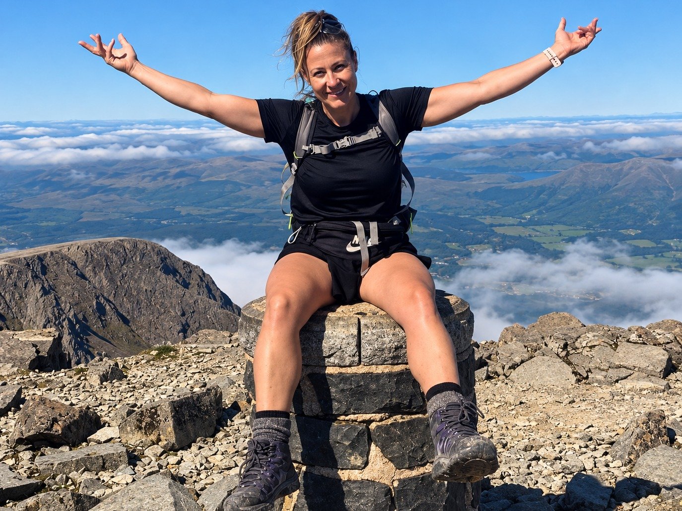 Linda Wilde on a mountain summit, arms open to the view.